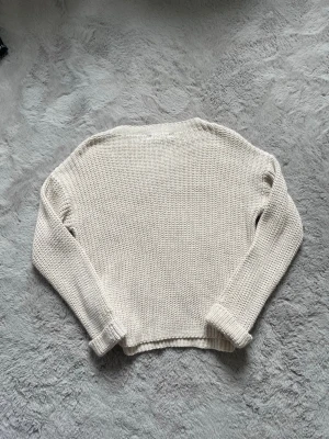 Beige stickad tröja från H&M - Säljer en beige stickad tröja från H&M med grovstickad struktur. Tröjan har långa ärmar, rund halsringning och ribbade muddar vid ärmslut och nederkant. Perfekt för lager på lager och enkel att matcha med olika stilar.