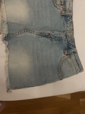 Ljusblå jeanskjol från True Religion - Ljusblå jeanskjol från True Religion med fransig kant och klassiska fickor både fram och bak. Kjolen är i storlek 25 och har normal passform, den är perfekt nu till sommaren ordinarie pris 1100 (vill jag minnas) säljer för 800. Endast använd ett få tal gånger då den e för liten. 