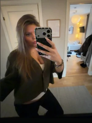 Olivgrön croppad kofta - Trendig olivgrön croppad kofta med långa ärmar och öppen framtill. Perfekt att slänga över ett linne eller t-shirt för en avslappnad men snygg look. Mjuk och skön, passar till både jeans och kjol.