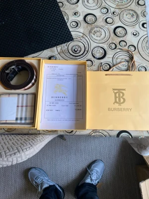 Burberry bälte med klassiskt rutmönster - Snyggt Burberry bälte i skinn med det ikoniska beigea, svarta och röda rutmönstret. Bältet har ett metallspänne med Burberrys logotyp och levereras i originalförpackning med dustbag och påse. Perfekt accessoar för att lyfta din outfit. Priset kan diskuteras 