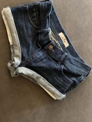 Hollister low waist shorts  - Snygga mörkblå jeansshorts från Hollister i storlek w24 med uppvikta benslut och klassisk femficksdesign. Shortsen har bälteshällor, knapp och dragkedja framtill. Perfekta för varma dagar och ger en avslappnad vibe.