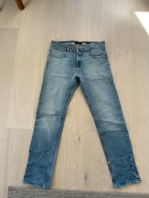 Ljusblå raka Massimo Dutti jeans  - Säljer ett par ljusblå jeans med rak passform och klassisk femficksdesign. Jeansen har subtila slitningar och en vintage tvätt som ger en avslappnad look. Perfekta för dig som gillar en enkel och tidlös stil.