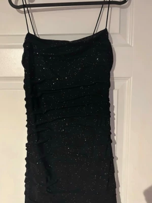 Svart glittrig festklänning med tunna band - Svart kort klänning med tunna axelband och glittriga detaljer som verkligen fångar ljuset. Figurnära passform som framhäver kroppen snyggt Den perfekta klänningen för utekväll, fest eller födelsedag 🖤✨(ifrån shein)