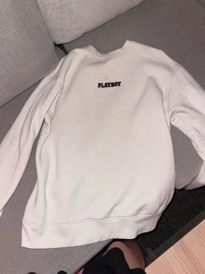 Vit sweatshirt från Playboy - Säljer en stilren vit oversized sweatshirt från Missguided Playboy med broderad logga på bröstet. Tröjan har rund halsringning, långa ärmar och mjukt, fleeceliknande material på insidan. Perfekt för dig som gillar enkel men snygg streetwear.