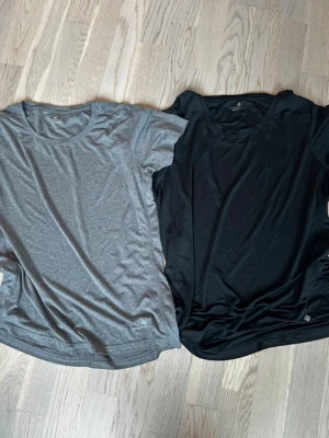 Två sportiga t-shirts i svart och grå - Säljer två sportiga t-shirts, en i svart och en i grått. Båda har rund halsringning och korta ärmar. Materialet känns lätt och andas, perfekt för träning eller aktiva dagar. Stilren design utan mönster eller detaljer. Rök och djurfritt hem. Pruta gärna !🌸