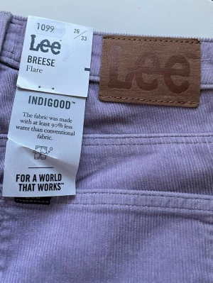 Lila manchesterbyxor från Lee  - Säljer ett par lila manchesterbyxor från Lee, modell Breeze Flare. Byxorna har utsvängda ben, klassisk femficksdesign och är tillverkade i ett tyg som sparar vatten. Perfekta för dig som gillar retrovibbar och vill sticka ut med färg. Helt nya med prislapp
