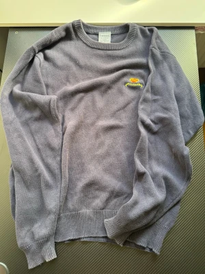 stickad tröja från Trimingham's - Säljer en stickad tröja från Trimingham's Bermuda i 100% fin bomull. Tröjan har rund halsringning, ribbade muddar och en liten broderad detalj med text och blomma på bröstet. Perfekt för dig som gillar stilrena och bekväma plagg.