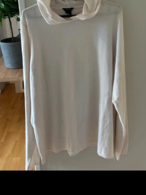 Vit stickad  hoodie med huva - Säljer en enkel och stilren hoodie med huva. Hoodien har långa ärmar och en avslappnad passform. Perfekt för dig som gillar en clean och basic look. Materialet ser ut att vara mjukt och bekvämt, troligen bomull eller bomullsblandning.