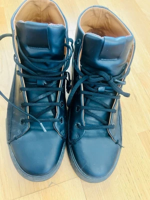 Svarta Zara High-top sneakers i läderimitation – Strl 41 - Säljer ett par snygga svarta high-top sneakers från Zara. Skorna är i bra skick och har en stilren design som passar till det mesta. Insidan är läderfärgad vilket ger en snygg kontrast.