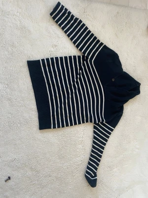 Marinblå randig stickad tröja Henri Lloyd - Säljer en marinblå stickad tröja från Henri LLoyd med vita horisontella ränder. Tröjan har lång ärm, bred ribbad mudd nedtill och vid ärmslut samt en hög krage med knappdetalj. Perfekt för dig som gillar klassisk och stilren look.