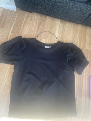 Svart puffärmad t-shirt från Monki - Svart t-shirt från Monki med puffiga korta ärmar och rund halsringning. Tillverkad i mjuk bomull som känns skön mot huden. Enkel men trendig design som passar till det mesta och har använt en gång max då den är som ny! Och storleken är M men ja har S och de passar mig!