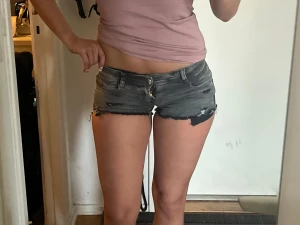 Grå slitna jeansshorts Lågmidjade  - Säljer ett par grå jeansshorts med låg midja och råa, fransiga kanter. Shortsen har slitningar och en klassisk femficksmodell med knappgylf. Perfekta för sommardagar och en avslappnad look. De sitter väldigt tajt på mig, skulle rekomendera de till någon som har Xs eller S.