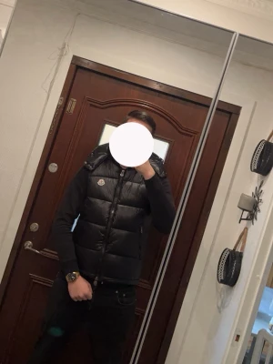 Svart dunväst från Moncler - Snygg svart dunväst från Moncler med hög krage och diskret logotyp på bröstet. Västen har en quiltad design och dragkedja framtill. Perfekt för lager-på-lager och ger en clean streetwear-look. Den är relativit ny och har qr skanning vid märket   