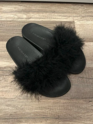 Svarta fluffiga tofflor från Primark - Ett par par svarta tofflor med bred rem i fluffigt fuskpälsmaterial från Primark i storlek 38. 