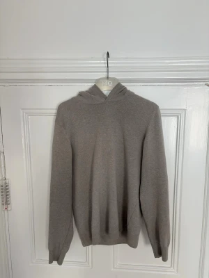 Beige hoodie i kashmir från Oscar Jacobson - Mjuk och stilren beige hoodie från Oscar Jacobson i kashmir. Hoodien har en klassisk huva, långa ärmar och ribbade muddar vid ärmslut och nederkant. Perfekt för dig som gillar en enkel men lyxig look.