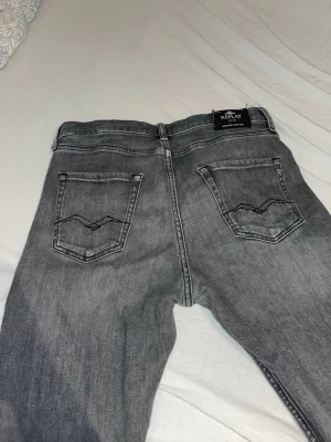 Grå jeans från Replay - Säljer ett par grå jeans från Replay med raka ben och klassisk femficksmodell. Jeansen har slitningar på framsidan och snygga detaljer på bakfickorna. Materialet är mjukt denim som ger en avslappnad look.