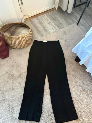 Svarta linnebyxor med raka ben - Säljer ett par svarta linnebyxor med hög midja och raka ben. Byxorna har en minimalistisk look och är perfekta för en clean och avslappnad stil. Tillverkade i ett svalt linnematerial som passar bra till sommaren. Enkla att matcha med olika toppar och skor.