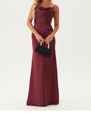 Vinröd balklänning  - Elegant vinröd långklänning med tunna axelband och draperad urringning. Klänningen har en figurnära passform och faller snyggt längs kroppen. Perfekt för bal eller festliga tillfällen.
