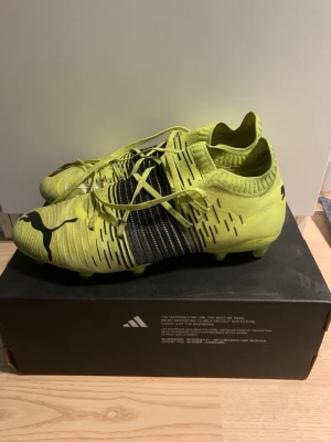 Gula Puma fotbollsskor med snörning - Säljer ett par gula fotbollsskor från Puma med svart logga och detaljer. Skorna har snörning, låg profil och stickad ovandel för bra passform. Sulan har fasta dobbar för spel på gräs. Säljer för dem är för små. Pris kan diskuteras box finns ej.