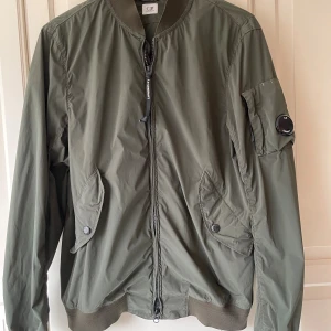 Bomberjacka / sommarjacka C.P. Company - C.P. Company klassisk bomberjacka i khakigrönt / militärgrönt  En tunn bomberjacka från det ikoniska märket C.P. Company – typ som en vindjacka, perfekt till vår och sommar eller över en hoodie. Riktigt snygg och i mycket gott skick, tyvärr lite för stor för mig så jag har köpt en mindre storlek istället. Mått: Axel t axel: 48 Ärm: 70 Rygg: 72