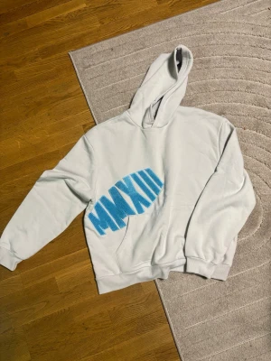 Vit hoodie från boohooMAN med blått tryck - Säljer en vit hoodie från boohooMAN med ett stort blått tryck i form av romerska siffror på framsidan. Hoodien har huva och magficka, samt ribbade muddar vid ärmslut och nederkant. Perfekt för en chill och avslappnad stil.