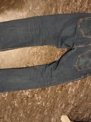 Blå jeans 405 Regular Fit 32/30 - Säljer ett par klassiska blå jeans från 405 med regular fit och raka ben. Jeansen har snygga bakfickor med kontrastsömmar och är tillverkade i slitstark denim. Perfekt för dig som gillar en enkel och tidlös look.