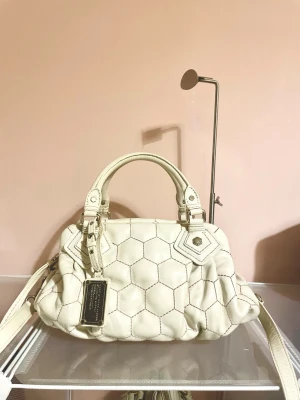 Vit handväska från Marc by Marc Jacobs - Snygg vit handväska från Marc Jacobs i mjukt läder med unikt hexagonmönster. Väskan har både handtag och axelrem samt en metallbricka med logga framtill. Perfekt för dig som vill ha en trendig och stilren accessoar.