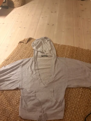 Ljusgrå hoodie från Atmosphere - Säljer en ljusgrå hoodie från Atmosphere med djup V-ringning och ribbade kanter. Hoodien har en huva och dragsko i midjan för en snygg passform. Tillverkad i mjukt, tunt material som känns skönt mot huden. Perfekt för en avslappnad och trendig look.
