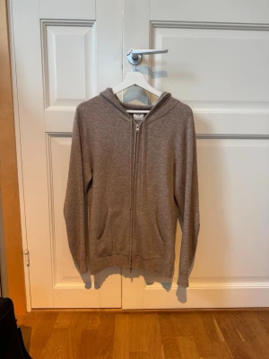 John Henric Kashmir hoodie  - Beige hoodie från John Henric med dragkedja framtill och två fickor. Tillverkad i kashmir, klassisk passform med huva och långa ärmar. Perfekt för chill dagar eller när du vill vara extra bekväm. Den är i allmänt fint skick förutom två hål (visas på bilderna). Hör av dig vid minsta fundering, pris kan diskuteras!