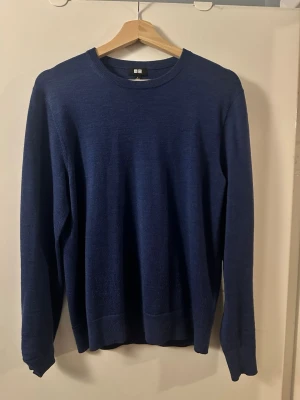 Merinoull mörkblå stickad tröja Uniqlo - Snygg mörkblå stickad tröja från Uniqlo med rund halsringning och långa ärmar. Tröjan har en enkel och stilren design, perfekt att matcha med jeans eller kjol. Materialet ser ut att vara mjukt och bekvämt, troligen bomull eller ullblandning.