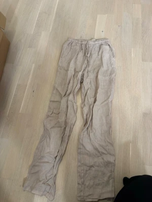 Beige linnebyxor från Design by Si - Säljer ett par beige linnebyxor från Design by Si. Byxorna har resårmidja med dragsko och raka ben. Tillverkade i ett luftigt linnematerial som passar perfekt till sommaren. Snyggt avslappnad look och neutrala färger som är lätta att matcha.