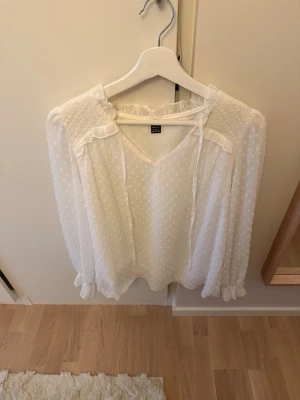 Vit prickig blus - Söt vit blus från H&M med diskreta prickar och volangdetaljer på ärmarna. Blusen har v-ringning med knytband om man vill knyta. Jättefin! Använt endast 1 gång!💕