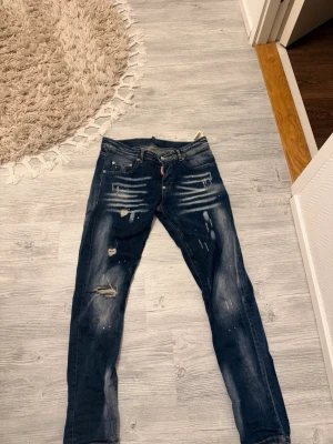 Dsquared2 jeans - Säljer ett par mörkblå jeans med slitningar, hål och coola blekta detaljer på låren och knäna. Jeansen har klassisk femficksdesign och är i denim. Perfekta för dig som gillar en streetig och avslappnad stil.