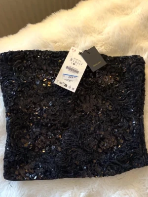 Svart paljett-tubtopp - Snygg svart tubtopp från Zara täckt med glittrande paljetter och broderade detaljer. Perfekt för dig som vill sticka ut och addera lite extra bling till din outfit. Toppen har en åtsittande passform och är stretchig för bästa komfort.