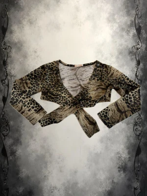 Leopardmönstrad bolero - Cool croppad omlottopp med leopardmönster och knyt framtill. Toppen har lång ärm och djup v-ringning, perfekt för att skapa en edgy look. Materialet känns mjukt och stretchigt, vilket gör den bekväm att bära.