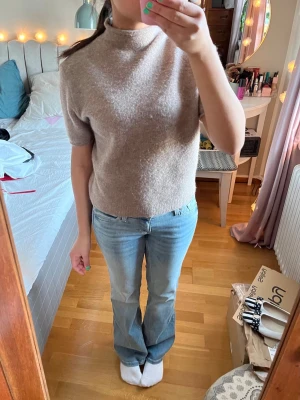 Beige stickad polo med kort ärm - Mysig beige stickad topp med korta ärmar och hög hals. Nytt skick helt o använd. Den är i storlek XL men är väldigt lite för sin storlek o passar mig som vanligtvis bär S.