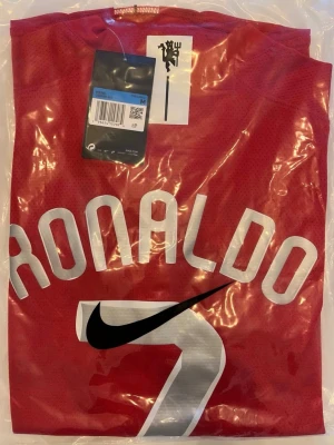 Manchester United Ronaldo tröja 2008 - Helt ny! Röd Manchester United matchtröja med Ronaldo och nummer 7 på ryggen. Tröjan har vit text, svart Nike-logga och är tillverkad i ett ventilerande funktionsmaterial. Perfekt för fotbollsträning eller att bära som supporter.