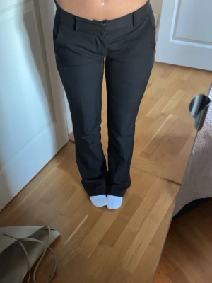 Svarta kostymbyxor med raka ben bikbok - Säljer ett par svarta kostymbyxor med raka ben och låg midja. Byxorna har två framfickor, bälteshällor och stängs med knapp och dragkedja. Klassisk och stilren modell som passar till många olika looks. Storlek 34