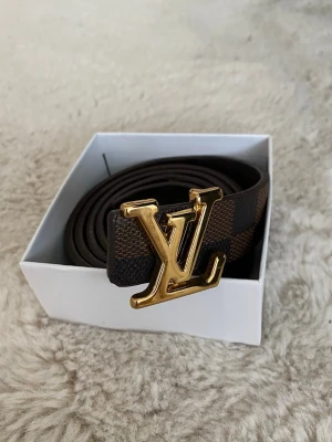  brunt bälte - Säljer ett brunt bälte med klassiskt rutigt mönster och ett stort, . Bältet är gjort i skinn och har en lyxig känsla som verkligen sticker ut. Perfekt accessoar för att lyfta vilken outfit som helst. Fick den som present och använder den inte längre det är bälte för kvinnor och den är small