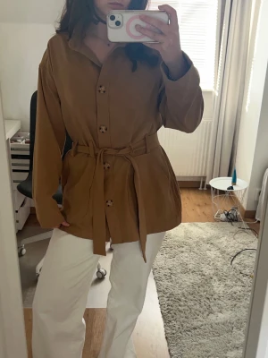 Brun / beige vårjacka - Snygg vår jacka med knappar och midjeband, sista bilden är baksidan av jackan men inget som syns tydligt.