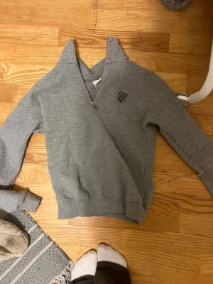 Grå halvzip hoodie från Maya Delorez - Snygg grå hoodie från Maya Delorez med halvzip och rund dragkedja. Tröjan har ribbade muddar vid ärmslut och nederkant samt en liten logga på bröstet. Tillverkad i mjukt sweatshirtmaterial som är skönt att ha på sig.