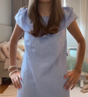 Blåvit randig kort klänning - Söt blåvit randig kort klänning med volang vid axlarna och ärmlös design. Perfekt för varma dagar och har en luftig passform. 