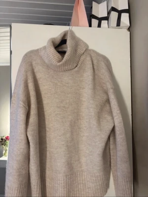 Beige polotröja från Gina Tricot - Mysig beige stickad polotröja från Gina Tricot i ullblandning. Tröjan har en hög, ribbstickad polokrage och breda ribbade muddar vid ärmslut och nederkant. Perfekt för kalla dagar och enkel att matcha med jeans eller andra byxor! Nästan aldrig använd därav priset.