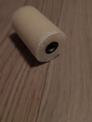 Beige skumgummi roller - En beige roller av skumgummi, perfekt för målning eller applicering av olika material. Cylindrisk form med metallfäste i mitten för enkel montering på ett handtag. Passar till pyssel, målning eller hobbyprojekt.