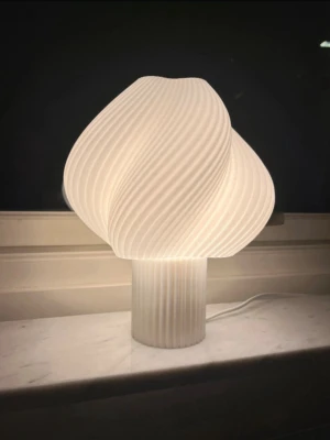 Créme/vit modern designlampa i 3D-print - Säljer en modern och stilren 3D-printad bordslampa med egendesignad form, tillverkad i vit PLA (en plast baserad på förnybara råvaror).   Lampan är även formgiven på insidan (se bild 2), vilket ger ett mjukare ljus och en mer exklusiv känsla.  Mått: Höjd: 27 cm Bredd: 24 cm  Tillverkad i tre delar: topp, botten samt hållare för ljuskälla (se bild 6).   Säljs utan glödlampa och sladd – standardkomponenter som enkelt kan köpas till. Sockel: E27 (standard). Rekommenderas att användas med LED-lampa.