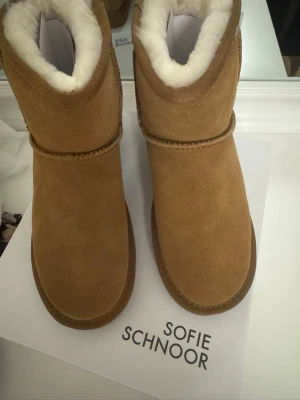 Bruna moon boots  - Säljer ett par snygga bruna moon boots från Sofie Schnoor. Boots i mocka-look med mjukt vitt foder och grov sula för bra grepp. Perfekta för kalla dagar när du vill hålla fötterna varma och stilen on point.