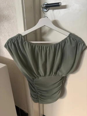 Grön omlott topp med rynkade detaljer - Snygg ljusgrön topp med omlott-design och rynkade detaljer i midjan. Toppen har korta ärmar och en bred, något fyrkantig ringning. Perfekt för dig som vill ha en trendig och stilren look.