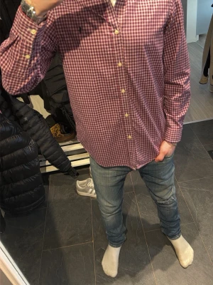 Rutig skjorta från Ralph Lauren - Säljer en klassisk röd och vit rutig skjorta från Ralph Lauren med button-down krage och broderad logga på bröstet. Skjortan har långa ärmar och knäppning framtill. Perfekt till jeans eller chinos för en clean och stilren look.