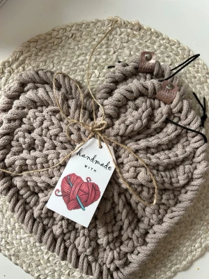 Handgjord beige virkade gryt underlägg  - Säljer 2 handgjorda virkade gryt underlägg  i tjockt beige garn. Underläggen  har grov struktur,  med läderdetaljer och etikett med texten 'handmade'.