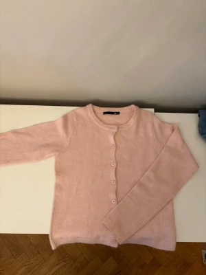 Ljusrosa kofta från lager 157 - Söt ljusrosa kofta från lager 157 med rund halsringning och knäppning framtill. Koftan har långa ärmar och är gjord i ett mjukt, tunt stickat material. 